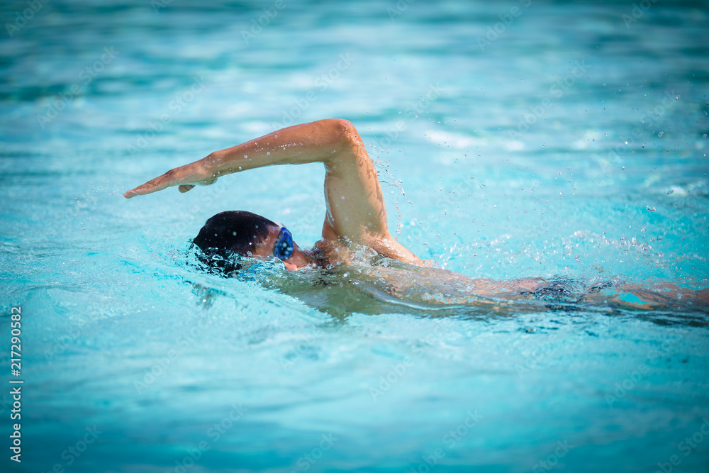 Man swimmer swimming crawl in a blue water  pool. Portrait of an athletic young male triathlete swimming crawl wearing swimming goggles. Triathlete training for triathlon.