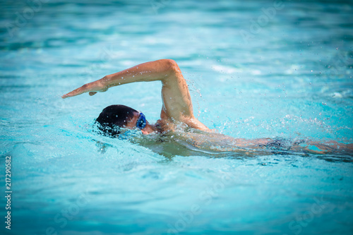 Man swimmer swimming crawl in a blue water  pool. Portrait of an athletic young male triathlete swimming crawl wearing swimming goggles. Triathlete training for triathlon. © lightpoet