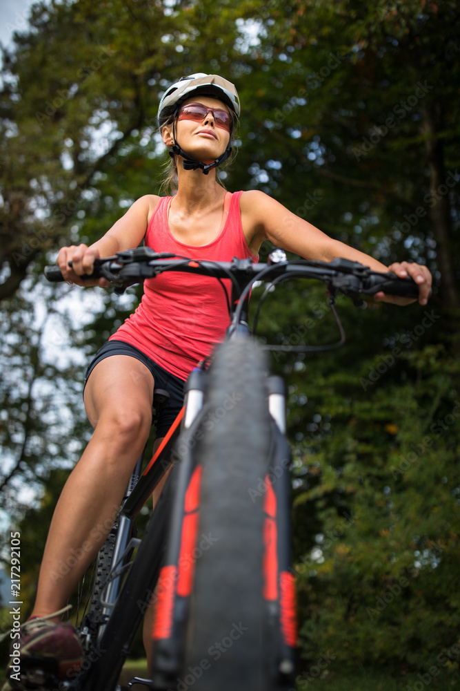 Fototapeta premium Pretty, young woman riding her mountain bike on a forest path. Enjoying active leisure time outdoors.