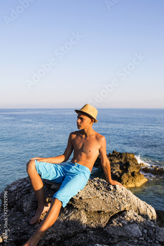  Teenager relaxing  on rocky coast at sea.