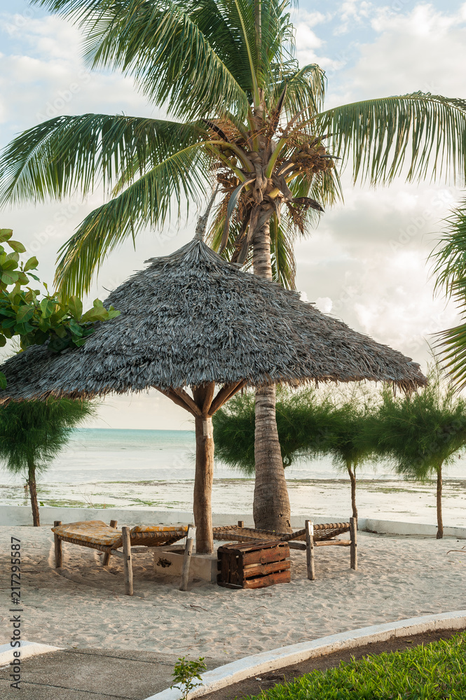 Sun loungers on the white sand and an umbrella of palm leaves in the Golden glow of the tropical sun