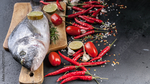 Fresh Dorado on a wooden cutting board. Aromatic herbs, lime, cherry tomatoes, salt, paprika and spices. Close-Up