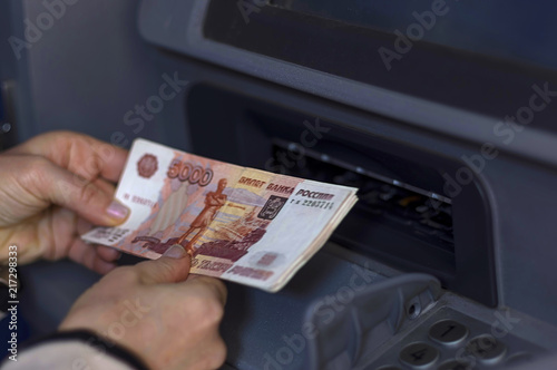 The hand holds a stack of money in front of the open ATM receive
