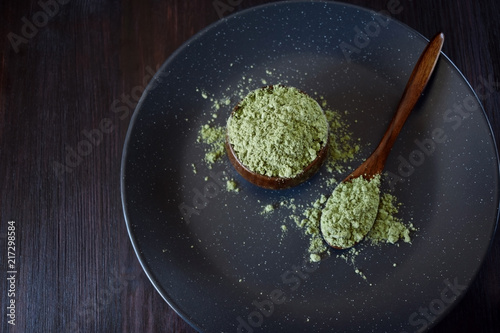Green matcha tea powder in a wooden bowl and spoon against the dark background