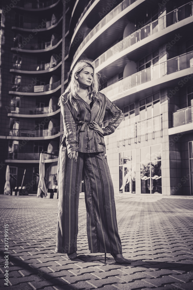 Beautiful girl in a stylish suit against a background of a blurry building. Stylish blonde. Fashionable girl. Everyday life of a beautiful girl. Lovely blonde in a stylish suit. Black and white. Beautiful girl in a stylish suit against a background of a blurry building. Stylish blonde. Fashionable girl. Everyday life of a beautiful girl. Lovely blonde in a stylish suit. Black and white.