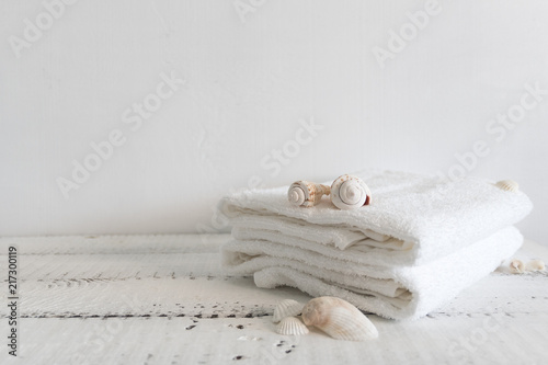 Folded white towels and different seashells on a white wooden table. Spa and wellness, cotton terry textile. Ecological theme © cathyrina