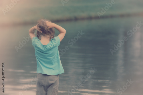 Little girl standing on a river bank with a wind in her hair