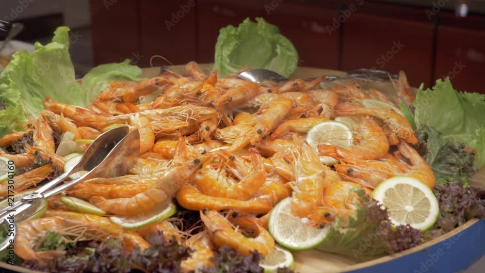 A closeup of a large dish full of cooked shrimps. It is decorated with lemon slices and lettuce leaves A closeup of a large dish full of cooked shrimps. It is decorated with lemon slices and lettuce leaves