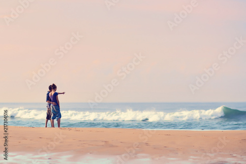 Young Couple standing on beach and looking to a sea. A man is showing his hand in the sea..