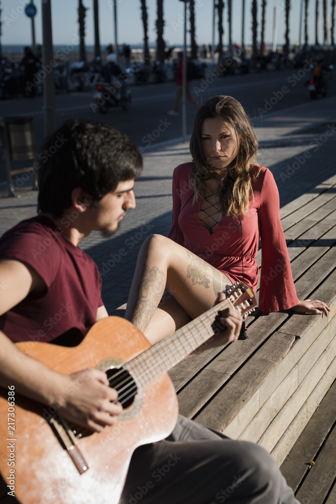 Spain, Barcelona, couple with a guitar sitting on a bench at seaside promenade