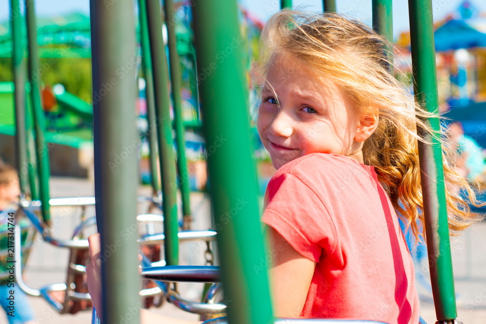 Joyful girl rides on a carousel and looks at the camera. Joyful girl rides on a carousel and looks at the camera.