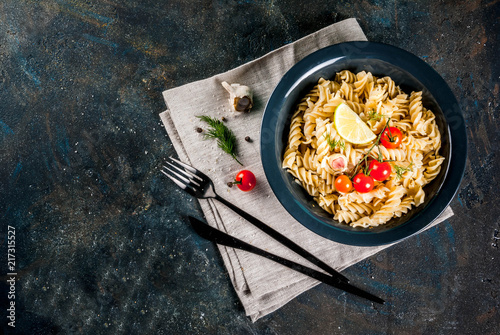 Classic italian pasta fusilli with pesto sauce, tomatoes, lime and fresh herbs in dark bowl, dark blue background copy space top view