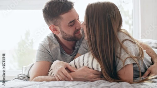 PAN of happy loving couple lying on bed and spending time together: they are rubbing noses and kissing gently