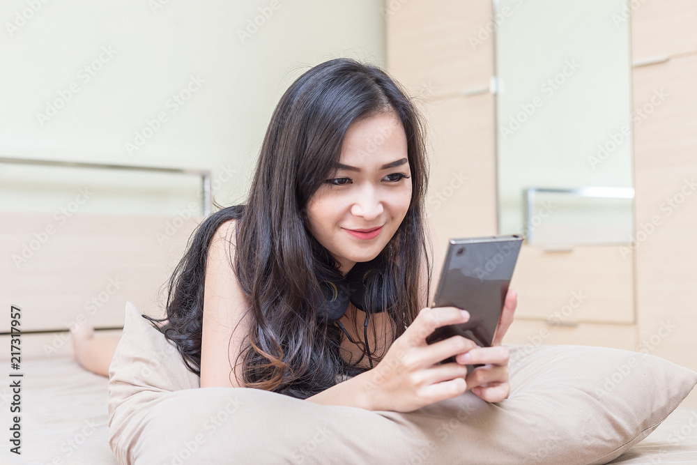 Beautiful Attractive Asian young woman lying on bed smile and using smartphone for playing social media in bedroom feeling so enjoy and relax Beautiful Attractive Asian young woman lying on bed smile and using smartphone for playing social media in bedroom feeling so enjoy and relax