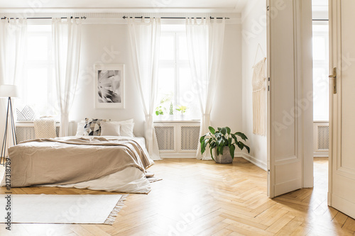 Spacious and bright bedroom interior with beige decorations, hardwood floor and a book on the window sill seat