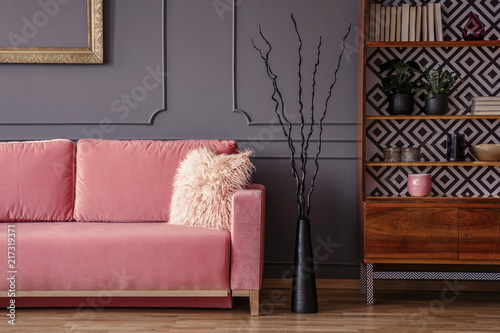 Pink sofa next to black decor and wooden cabinet in vintage living room interior. Real photo
