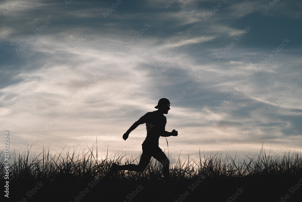 Silhouette of a man who runs through a meadow. A cloudy cloudy sky in the background