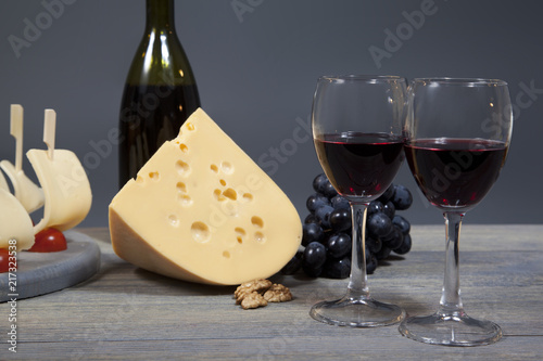 Two glasses with red wine on a wooden table. Cheese and bunch of grapes harmoniously complement the composition