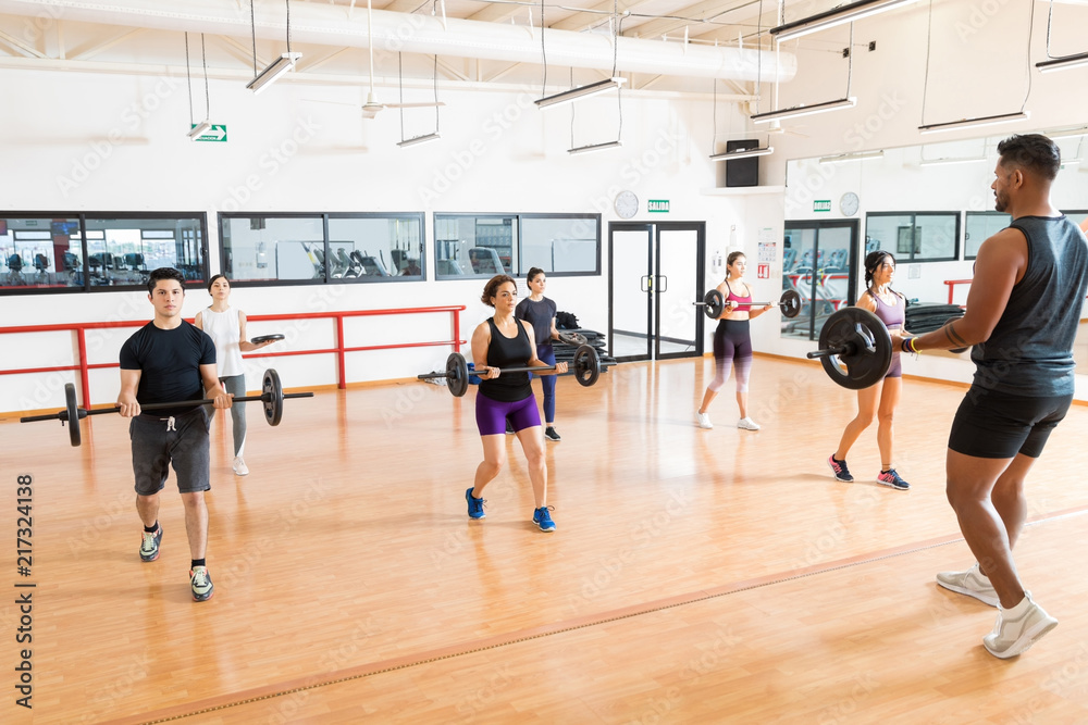 Instructor And Clients Lifting Barbells On In Gym