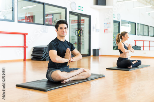 Confident Man With Hands Clasped Meditating With Friend In Gym