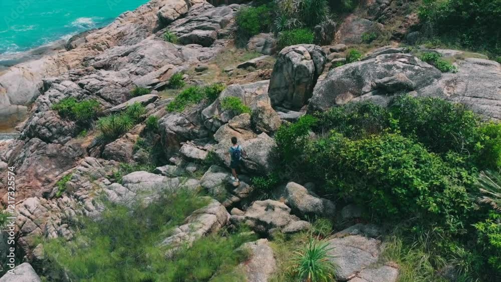 Hiker man trekking walking with backpack in trail at day time on big stony coast. Traveler man walking on stones Hiker man trekking walking with backpack in trail at day time on big stony coast. Traveler man walking on stones