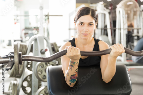 Confident Female Athlete Lifting Barbell Curl On Exercise Machine