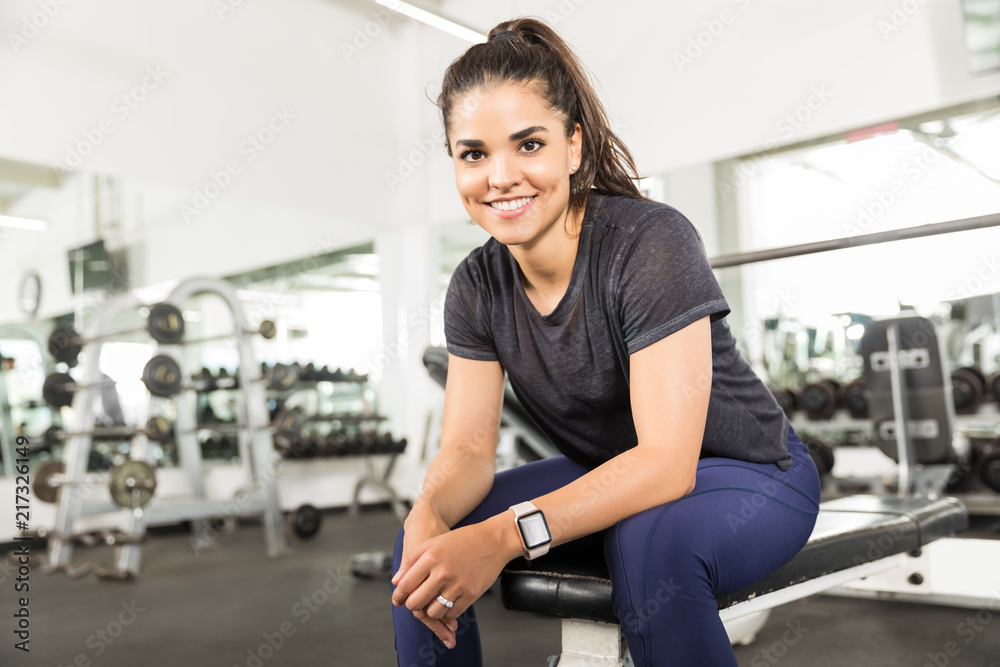 Fototapeta premium Smiling Healthy Female Sitting On Bench In Fitness Center