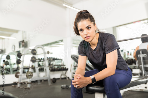 Confident Woman With Hands Clasped Relaxing On Bench At Gym