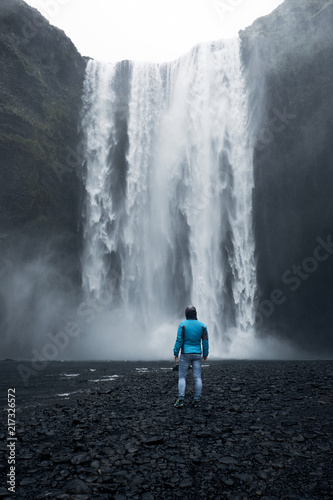 A person admirnig the beauty and the power of huge Skogafoss waterfall located in Iceland.