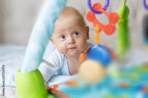 Charming baby in blue body, lies on the tummy and looks at the developing mat 
