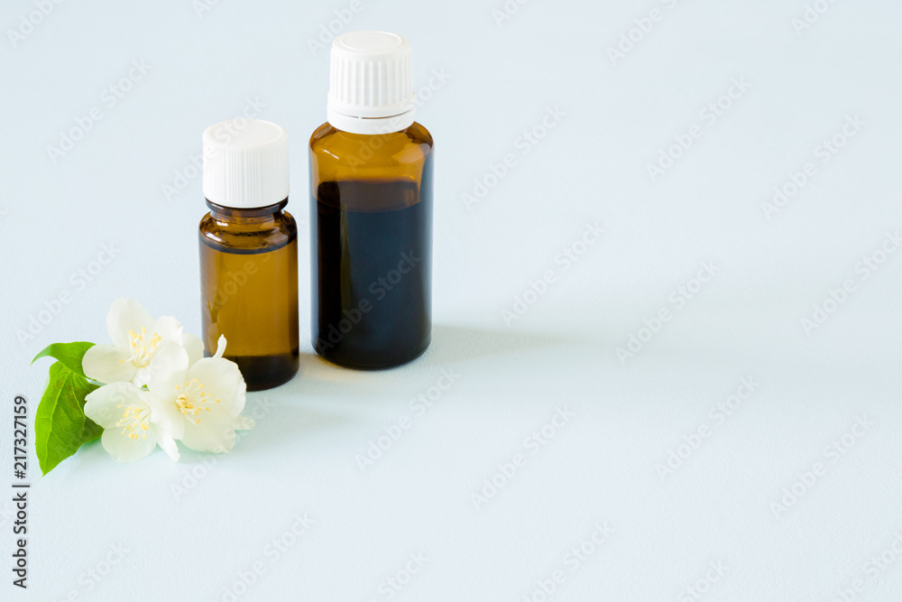 Small, brown glass bottles on pastel blue table. Essential oil with jasmine blossoms. Fresh, white flowers. Healthcare concept. Empty place for text or logo. Small, brown glass bottles on pastel blue table. Essential oil with jasmine blossoms. Fresh, white flowers. Healthcare concept. Empty place for text or logo.