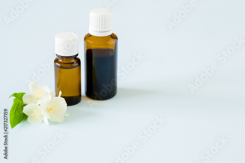 Small, brown glass bottles on pastel blue table. Essential oil with jasmine blossoms. Fresh, white flowers. Healthcare concept. Empty place for text or logo.