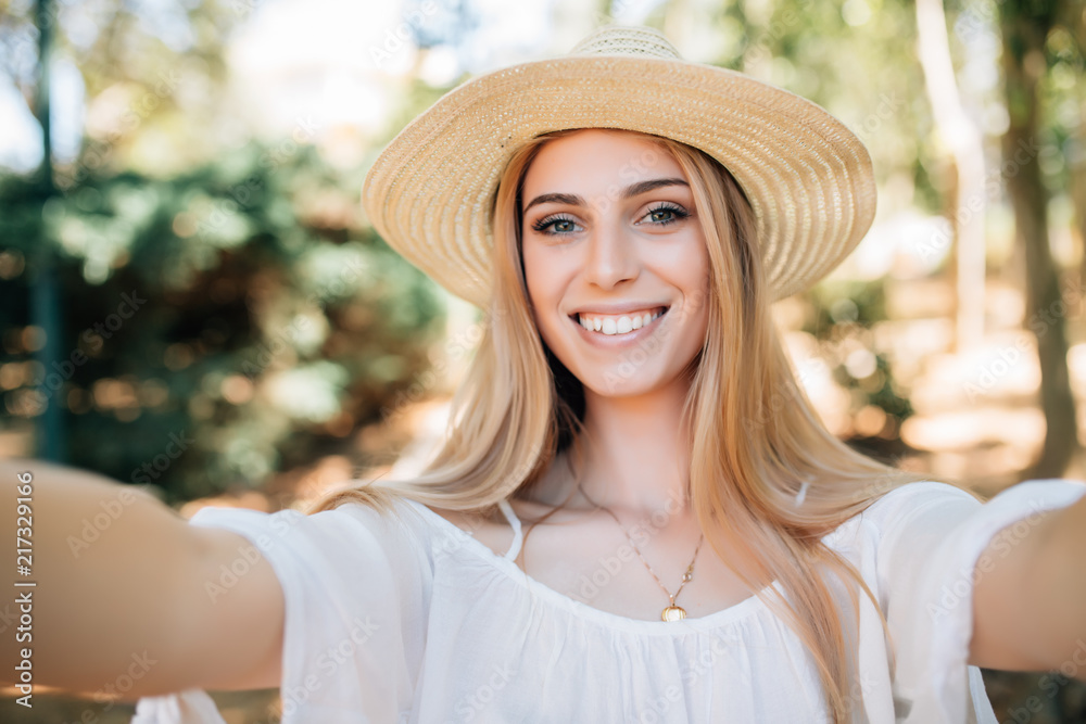 Portrait of happy woman wearing straw hat making selfie taking picture of herself in summer morning outdoors .