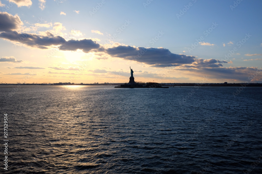 Hudson river view with the silhouette of the statue of Liberty against the blue sky and infinite horizon at sunset. New York City iconic tourist attraction.