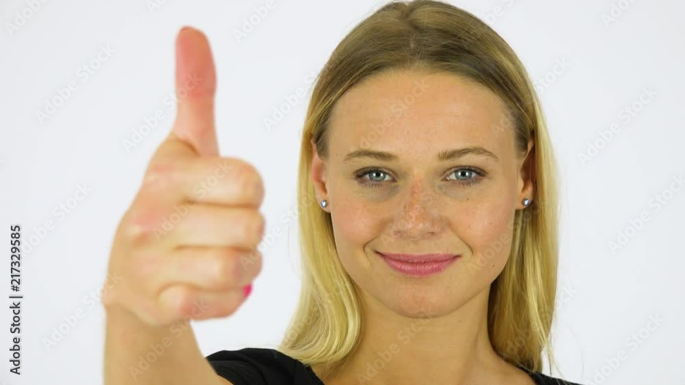 A young beautiful woman shows a thumb up to the camera with a smile - face closeup - white screen studio A young beautiful woman shows a thumb up to the camera with a smile - face closeup - white screen studio