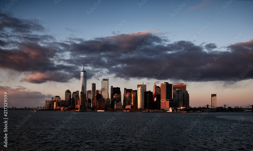 New York City skyline with urban skyscrapers over Hudson River at sunset. Manhattan downtown panorama. Waterfront view to the harbor at twilight.

