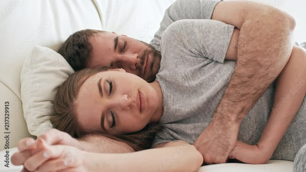 Handheld PAN of bearded man with closed eyes lying in bed and hugging beautiful girlfriend holding his hand Handheld PAN of bearded man with closed eyes lying in bed and hugging beautiful girlfriend holding his hand