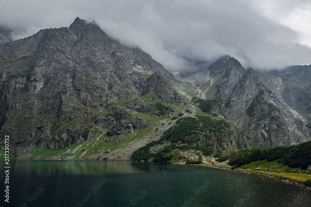 Beautiful view of foggy mountains cover by dark clouds and green forest with a reflection in a lake. Morskie Oko. Marine Eye. High Tatras, Zakopane, Poland