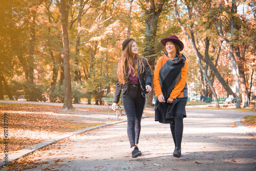 Two teenage girls are having fun in the park, autumn outfit. Funny girl friends throwing dry leaves in the city in autumn. Happy family on autumn walk!