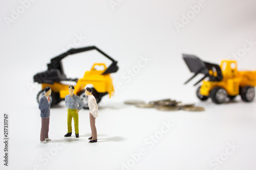 three miniature businessman with construction car and coins background.
