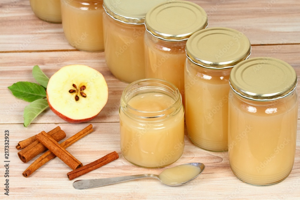 Homemade preserved apple puree in jars / Opened small jar in middle and apples on wooden board Homemade preserved apple puree in jars / Opened small jar in middle and apples on wooden board