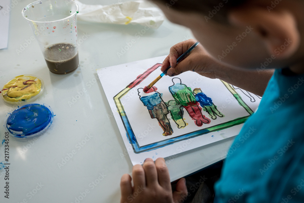 Naklejka premium Young boy coloring in an outline sketch with paint