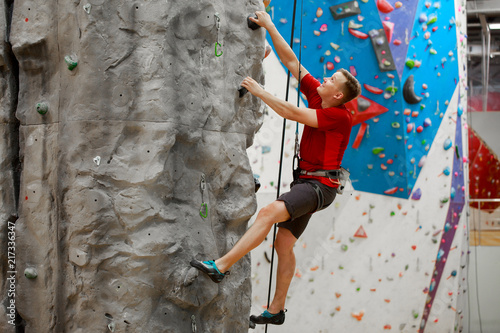 Photo from side of young sportsman exercising on climbing wall