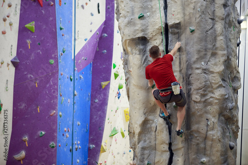 Photo from back of sportsman climbing up boulder in gym