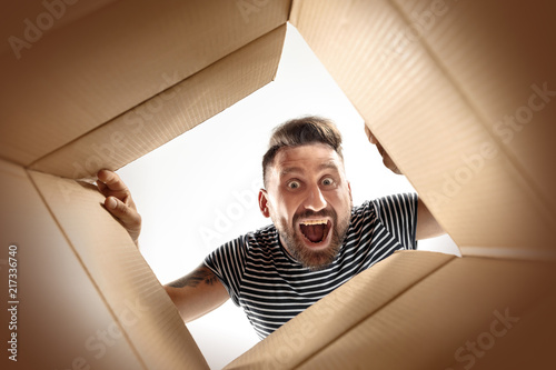 The surprised man unpacking, opening carton box and looking inside. The package, delivery, surprise, gift lifestyle concept. Human emotions and facial expressions concepts