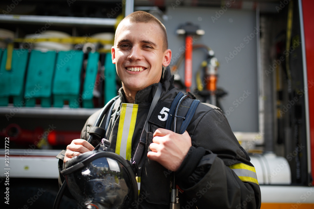 Obraz premium Photo of happy firefighter standing near fire truck with fire hose