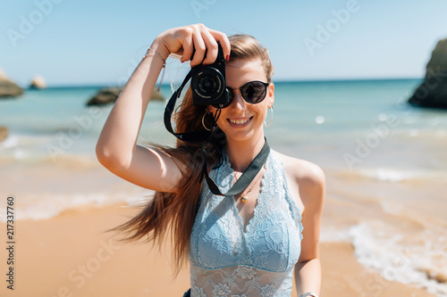 Happy woman on vacation photographing with a camera on the beach and smiling © dianagrytsku