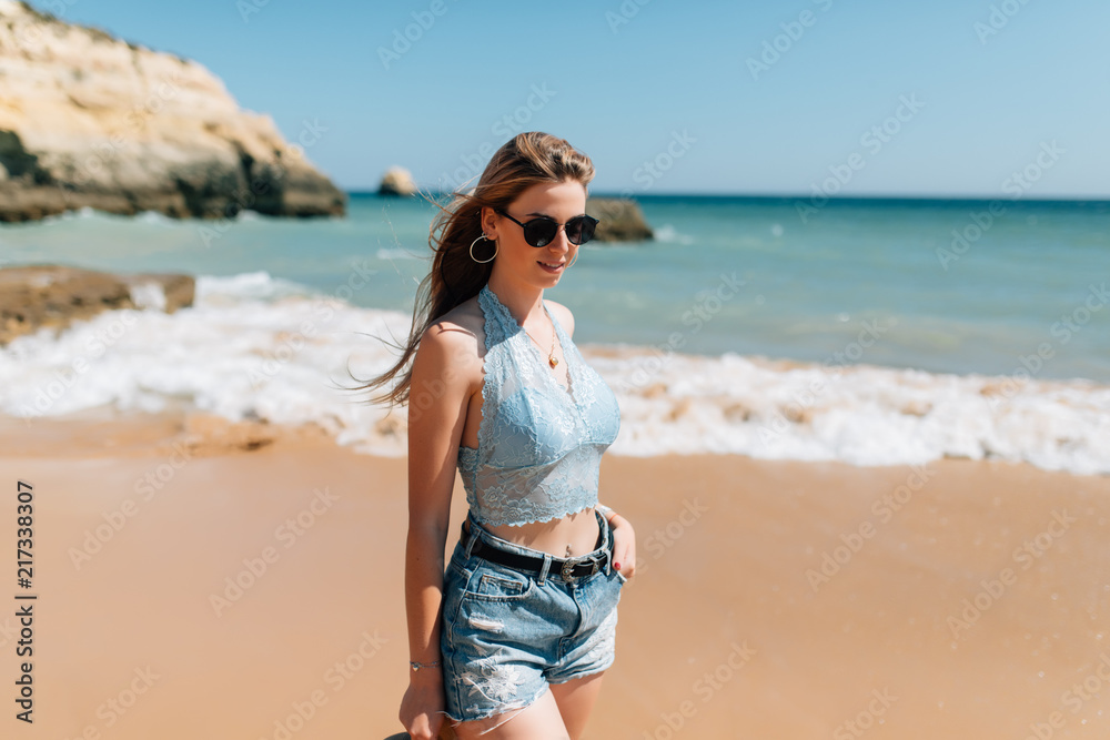 Young woman in sunglasses walking along the beach in sunny day Young woman in sunglasses walking along the beach in sunny day