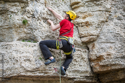 Photo from back of climbing sports man in yellow helmet on rock