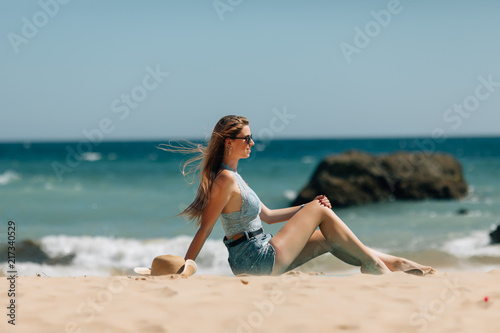 Wallpaper Mural Side view an attractive young woman wearing straw hat and sunglesses sits on a beach with ocean background Torontodigital.ca